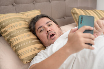 A lazy man in his 30s is annoyed after being told to get up. A bum lying on the bed chatting on the phone.