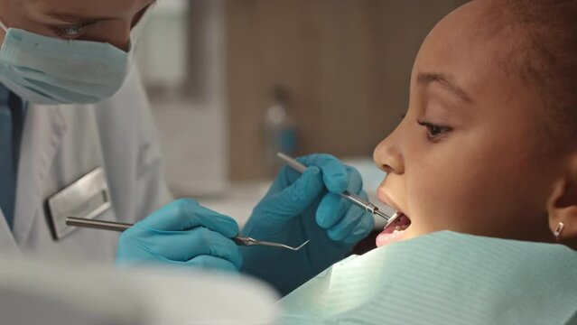 Medium closeup of African American little girl getting her teeth examined by female pediatric dentist at dental clinic