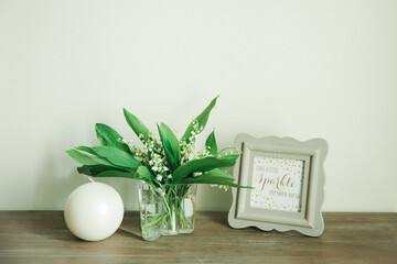 Lily of the valley in glass vase and photo frame on wooden table