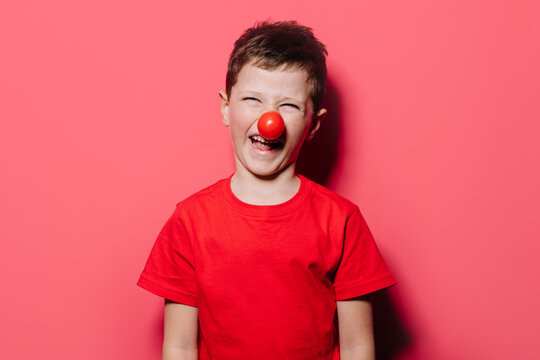 Humorous boy in casual red shirt with red poky nose posture in studio photo