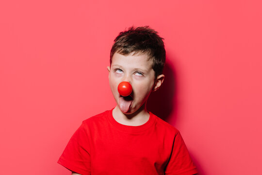 Humorous boy in casual red shirt with red poky nose posture in studio photo