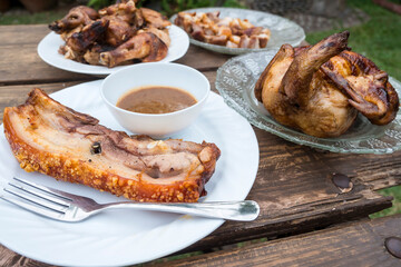 Plates of Lechon Manok or roasted chicken and Liempo or grilled pork belly, popular Filipino food served outside at a bench with gravy.