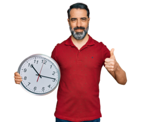 Middle aged man with beard holding big clock smiling happy and positive, thumb up doing excellent and approval sign