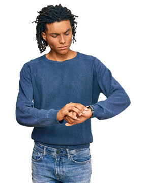 Young african american man wearing casual winter sweater checking the time on wrist watch, relaxed and confident