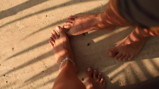 Couple is standing on bare feet on sand. Camera from above only takes pictures of people's feet. Love and tenderness. 