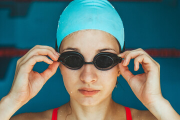 Extreme close-up shot of a Caucasian girl head with a swimming cap and hands putting swimming goggles, preparing for training in the pool.