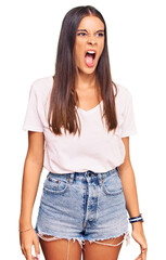 Fototapeta premium Young hispanic woman wearing casual white tshirt angry and mad screaming frustrated and furious, shouting with anger. rage and aggressive concept.