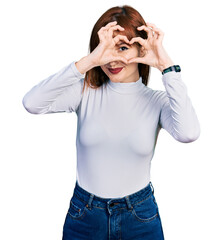 Redhead young woman wearing casual turtleneck sweater doing heart shape with hand and fingers smiling looking through sign