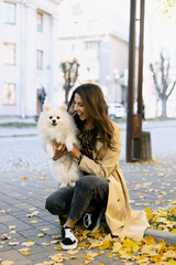 Attractive, young girl holds a beautiful dog in her arms, on the street. Smiling girl holding her pet, fallen leaves, autumn.