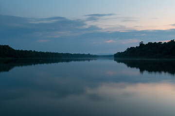 Fototapeta na wymiar Landscape of cloudy twilight with symmetric reflection on water surface, distant mountain in haze