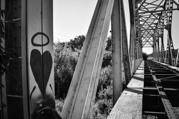 Black and white. Abandoned old Railway over the river bridge with heart shaped graffiti in the in...