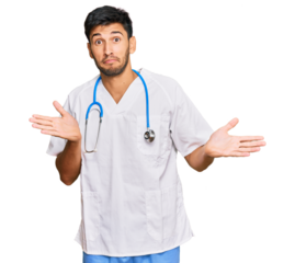 Young handsome man wearing doctor uniform and stethoscope clueless and confused expression with arms and hands raised. doubt concept.