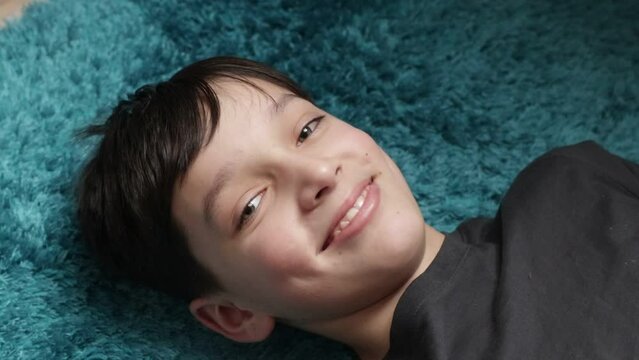 Video close up little brunette boy looking and camera and laughing, talking something, lying down on blue soft blanket