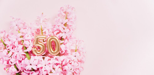 Number 50 fifty golden celebration birthday candle on Pink flowers Background. 50 years birthday. concept of celebrating birthday, anniversary, important date, holiday hyacinth bouquet. space for text