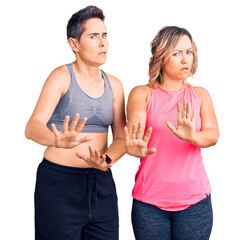 Couple of women wearing sportswear moving away hands palms showing refusal and denial with afraid...