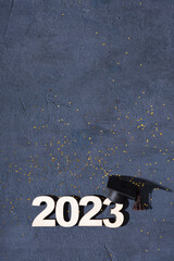 Class of 2023 concept. Wooden number 2023 with graduate statuette on concrete background with...