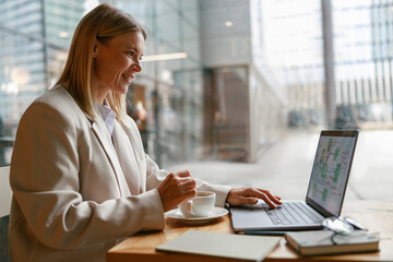 Woman freelancer working on laptop and drinking coffee while sitting in cafe near window