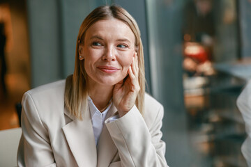 Close up portrait of attractive smiling businesswoman in jacket sitting in cafe and looking at side