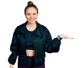 Young hispanic girl wearing sportswear smiling cheerful presenting and pointing with palm of hand looking at the camera.