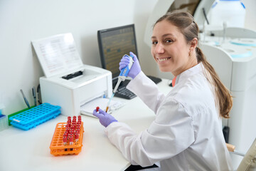 Smiling laboratory employee at her workplace works with blood samples