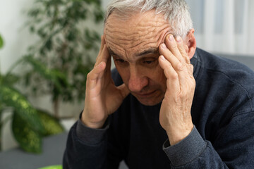 Senior man having headache and touching his head while suffering from a migraine in the living...