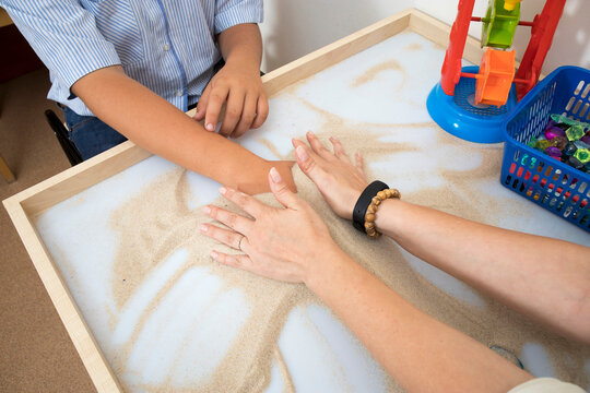 Fragment. Therapeutic activities with children. A doctor helps a patient with autism play with sand.