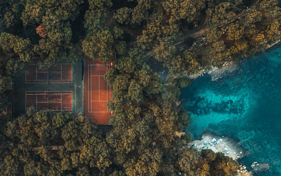 Top-down aerial view of Marjan Hill in Split, Croatia. The photo features a tennis court nestled among trees and an inviting beach exit. A perfect representation of Croatia's natural beauty.