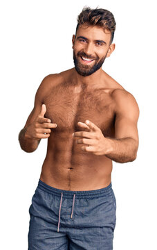 Young hispanic man wearing swimwear shirtless pointing fingers to camera with happy and funny face. good energy and vibes.