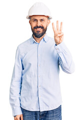 Young handsome man wearing architect hardhat showing and pointing up with fingers number three while smiling confident and happy.