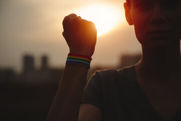 Pride parade, lgbtq woman with rainbow whirstband making fist sign st sunset