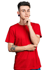 Young caucasian boy with ears dilation wearing casual red t shirt smiling looking confident at the camera with crossed arms and hand on chin. thinking positive.