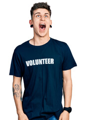 Young caucasian boy with ears dilation wearing volunteer t shirt angry and mad screaming frustrated and furious, shouting with anger. rage and aggressive concept.