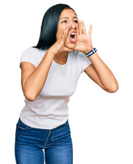 Beautiful hispanic woman wearing casual white tshirt shouting angry out loud with hands over mouth