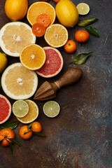 Set of various fresh citrus fruits with leaves and wooden juicer on dark concrete background. Healthy food backround. Flat composition with copy space. Top view