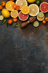 Set of various fresh citrus fruits with leaves and wooden juicer on dark concrete background. Healthy food backround. Flat composition with copy space. Overhead view