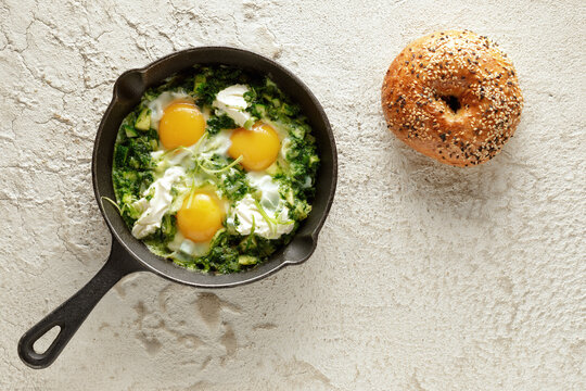 Green shakshuka with frshly baked bagel. Fried eggs in a cast iron pan. Traditional meal of the Jewish cuisine