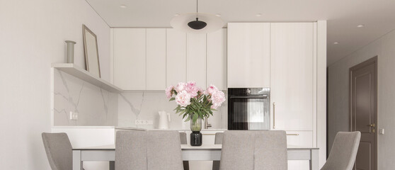 Warm white kitchen interior design, grey chairs, oak floor, rose peony in glass vase on dining table. Modern kitchen interior concept