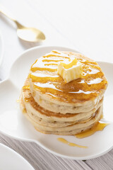 Pancake with butter and honey maple syrup set on white cafe table.