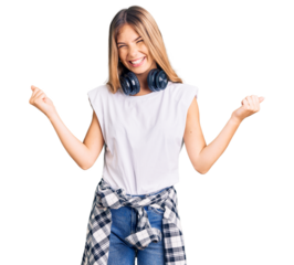 Beautiful caucasian woman with blonde hair listening to music wearing headphones very happy and excited doing winner gesture with arms raised, smiling and screaming for success. celebration concept.