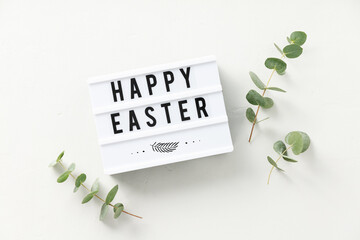 Easter composition, greeting card with lightbox text Happy Easter and eucalyptus branches on light...
