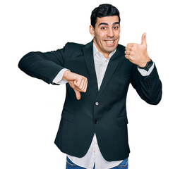 Handsome hispanic man wearing business clothes doing thumbs up and down, disagreement and agreement expression. crazy conflict
