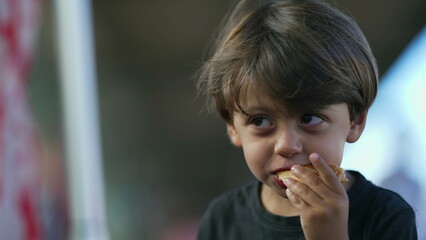 Fototapeta na wymiar One cute small boy eating piece of bread outside. Child eats snack