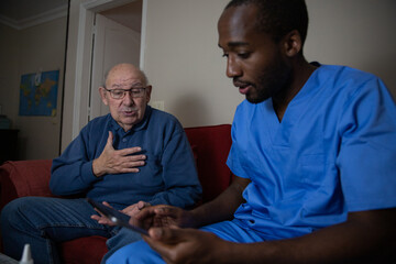 An elderly patient touches his chest in pain during a home doctor visit