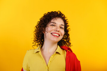 Studio shot of positive and smiling pretty female. Curly laughing girl in bright yellow shirt. Isolated on yellow background. Close up. Copy space.