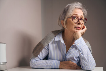 Beautiful elderly woman sits at home at the kitchen table