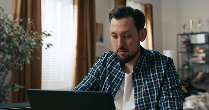 Close up shot concentrated beard young man working online with computer at home from distance. Person with disabilities.