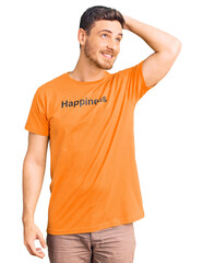 Obraz premium Handsome young man with bear wearing tshirt with happiness word message smiling confident touching hair with hand up gesture, posing attractive and fashionable