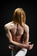 Obraz premium Young athletic professional ballet dancer with a bare torso and white dance tights is in perfect shape, performing and posing over a black background.