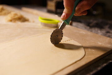 Cook cutting dough with cutter tool. Italian chef cooking pasta in the kitchen