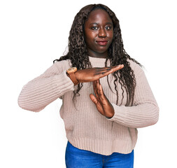 Young african woman wearing wool winter sweater doing time out gesture with hands, frustrated and...